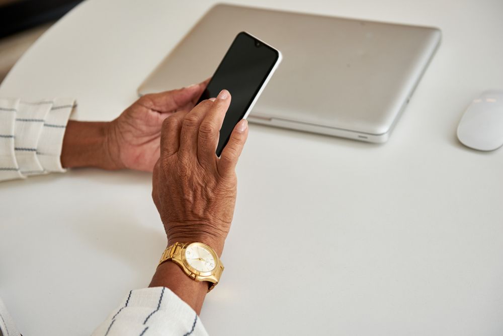 Hand eines älteren Menschen mit Smartphone am Schreibtisch